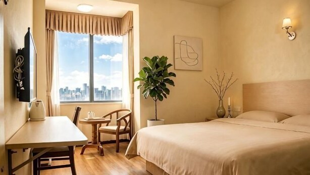 A hotel room with a bed, a desk, a chair, a window with a city view, and a plant. - Haojia Express Hotel (Zhuhai Gongbei Port Fuhuali Branch) (Zhuhai)