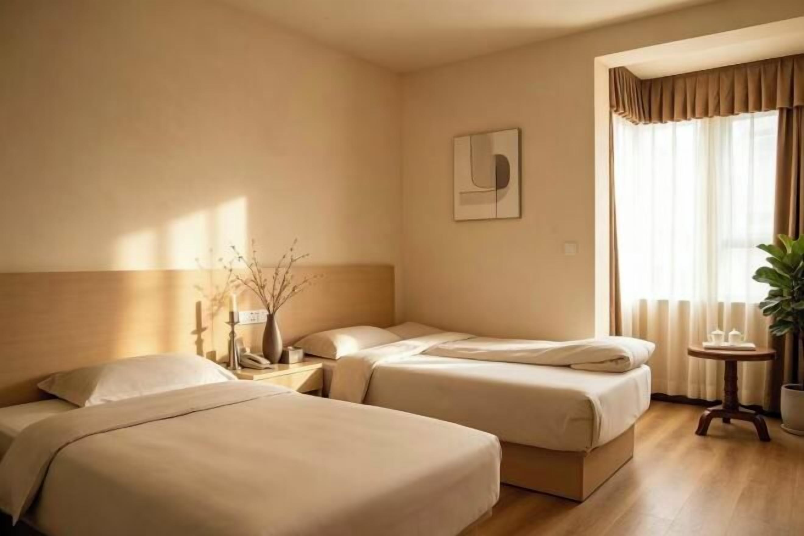 Een hotelkamer met twee bedden, nachtkastjes, een klein tafeltje met een plant en een raam met gordijnen.