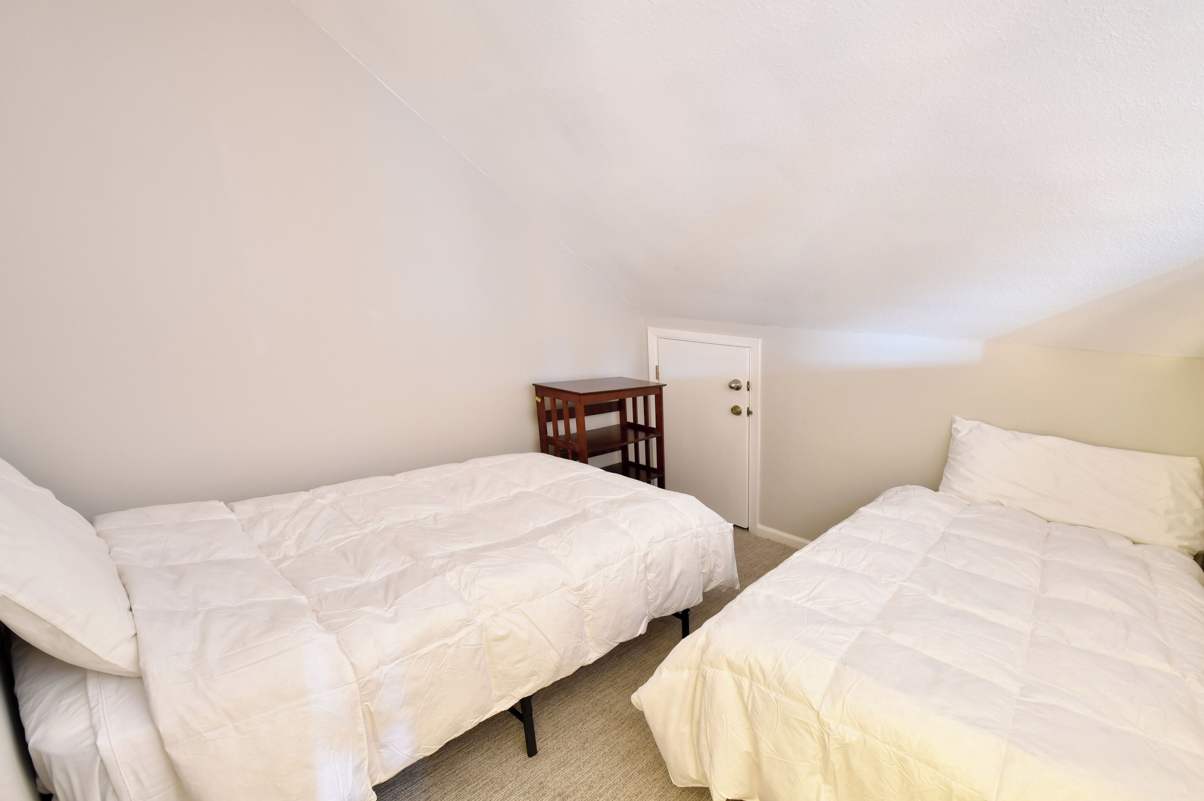 A small, single-room bedroom with two beds, a wooden chair, and a door.