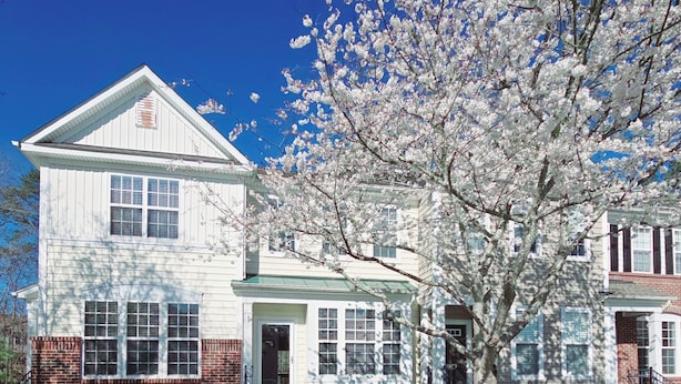 A two-story house with a front porch, a small front yard, and a tree with white blossoms. - The secret Manor (Durham)