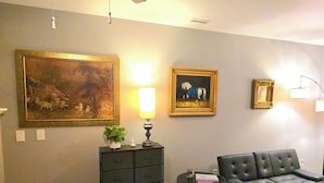 A living room with a black leather sofa, a small side table with a lamp, a cabinet, and two framed pictures on the wall. - The secret Manor (Durham)