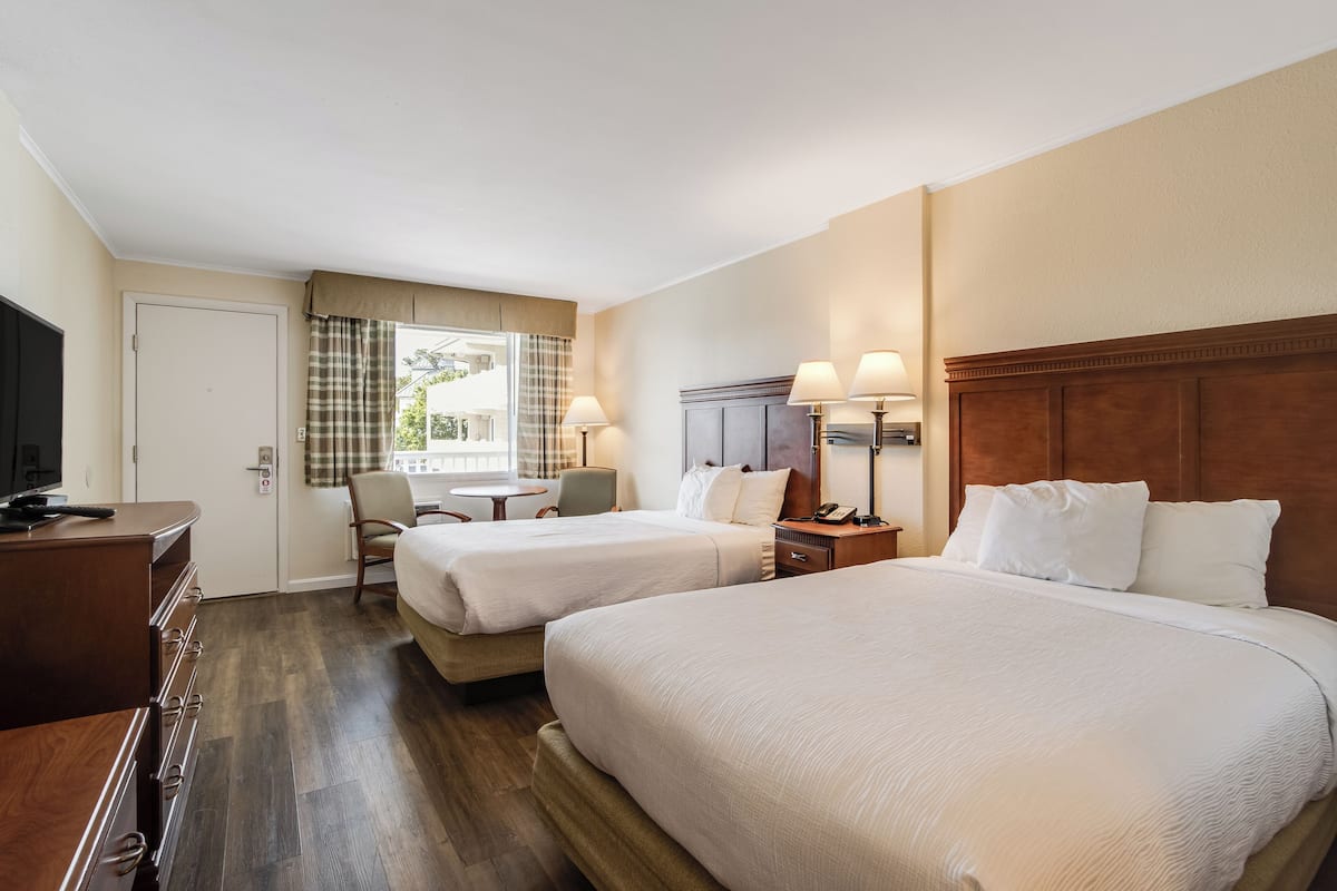 A hotel room with two beds, a desk, a chair, a TV, and a window with curtains.