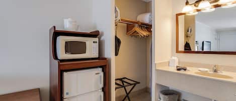 A compact bathroom with a white sink, a mirror with lights, a microwave, and a small refrigerator.