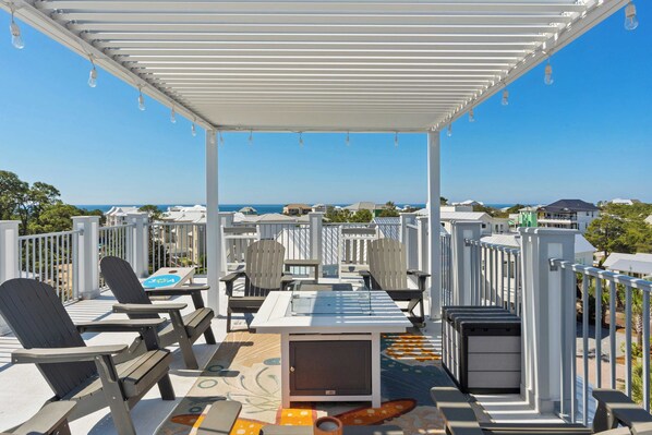 Un espace extérieur aménagé avec des sièges couverts, comprenant des fauteuils Adirondack et une table, offrant une vue sur la côte.