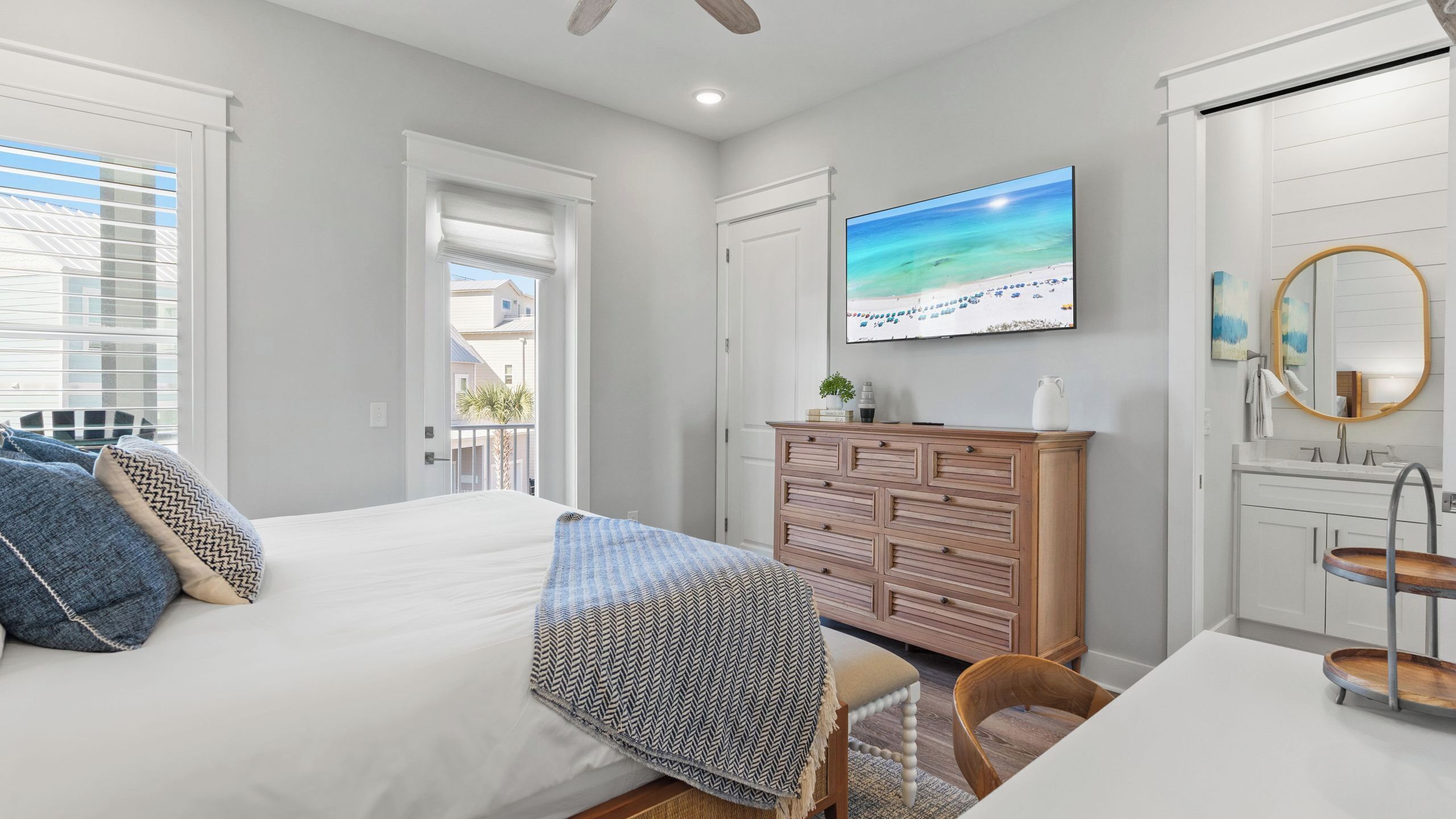 A bedroom with a bed, dresser, TV, and a view of the outside.