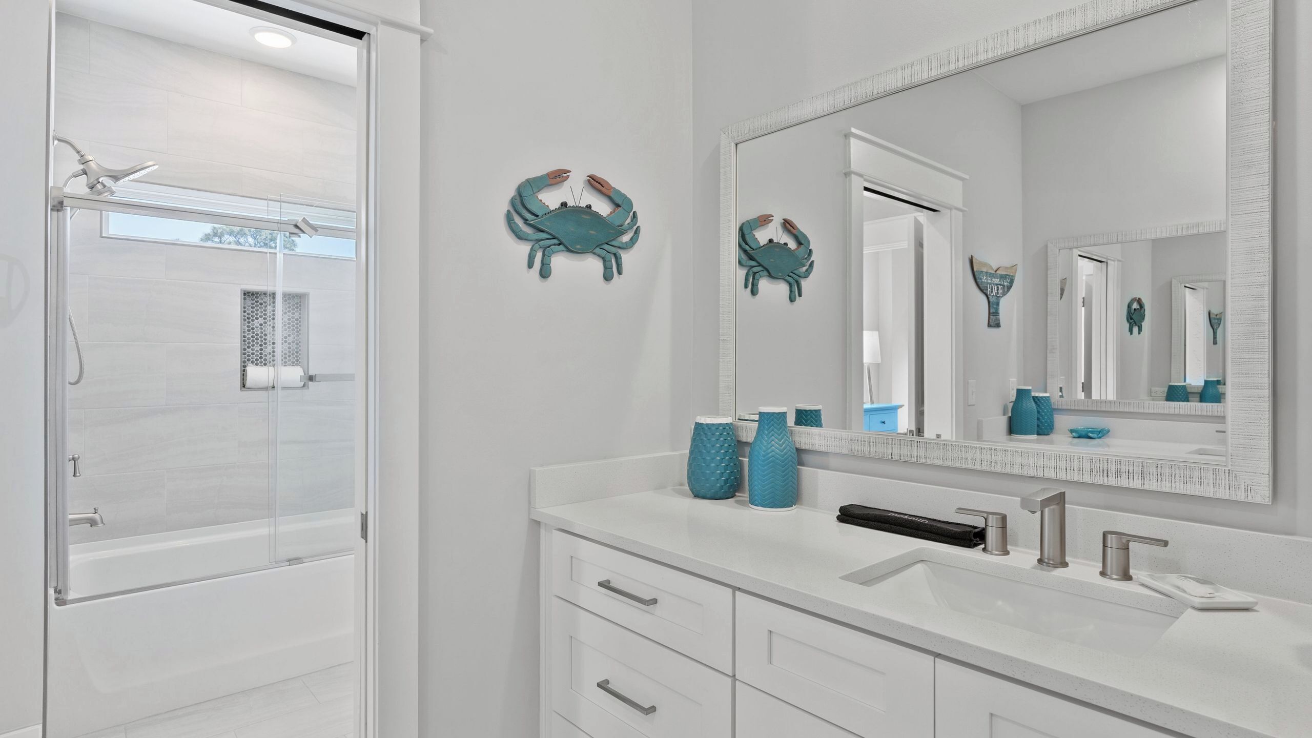 Een moderne badkamer met een douchecabine van glas, een grote spiegel en een witte wastafel met een wastafel en lades.