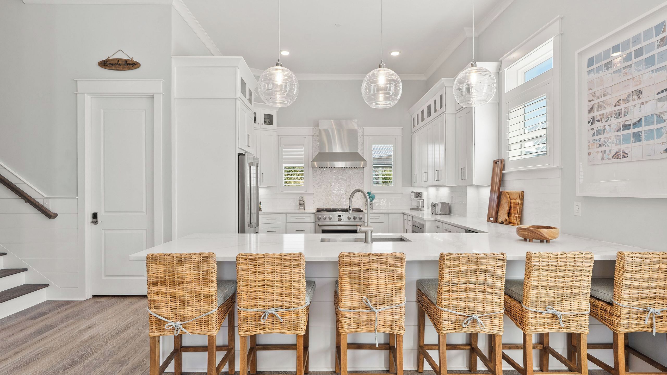 A modern kitchen with white cabinetry, a central island, and wicker bar stools.