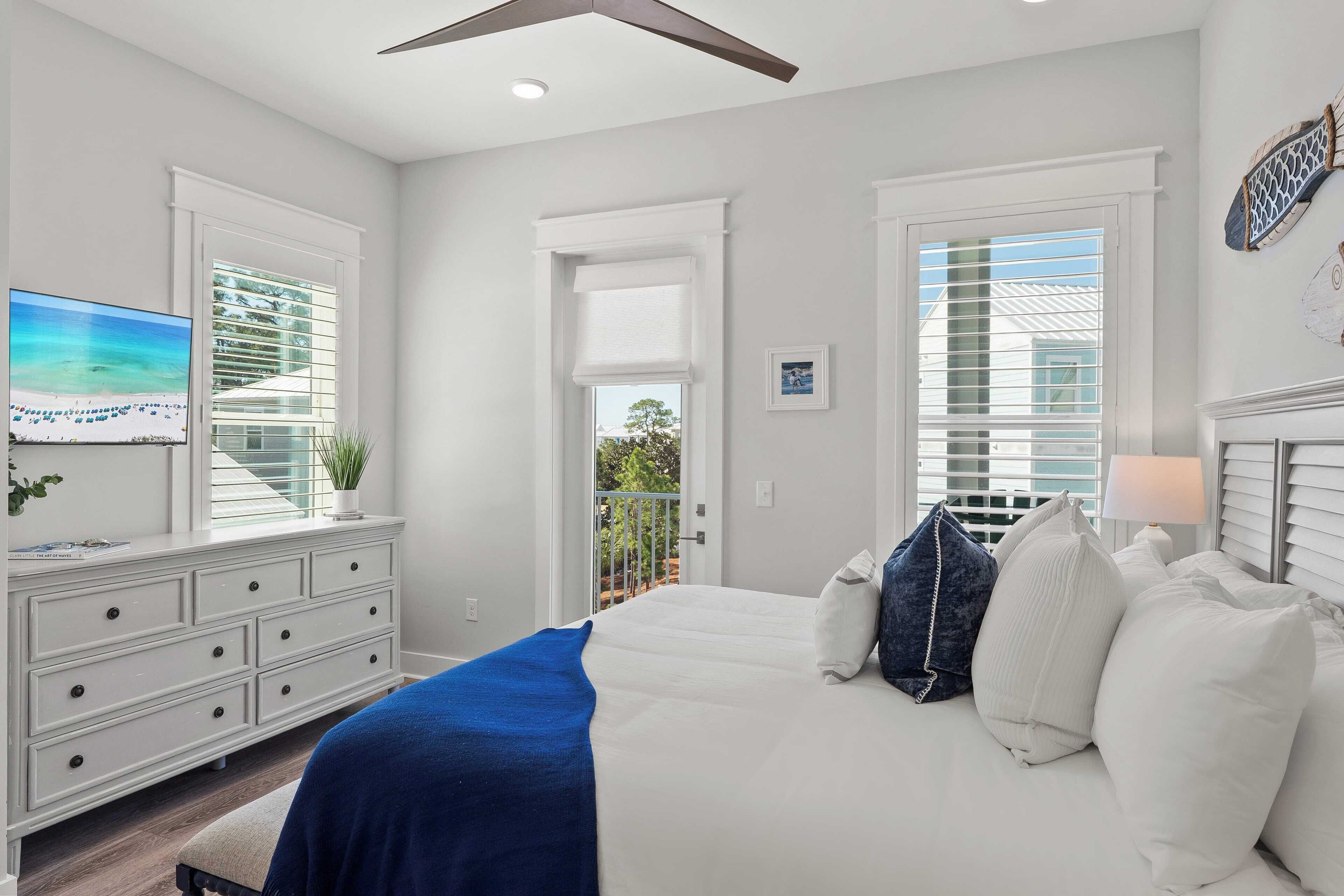 A bedroom with a bed, a dresser, a TV, and a balcony.