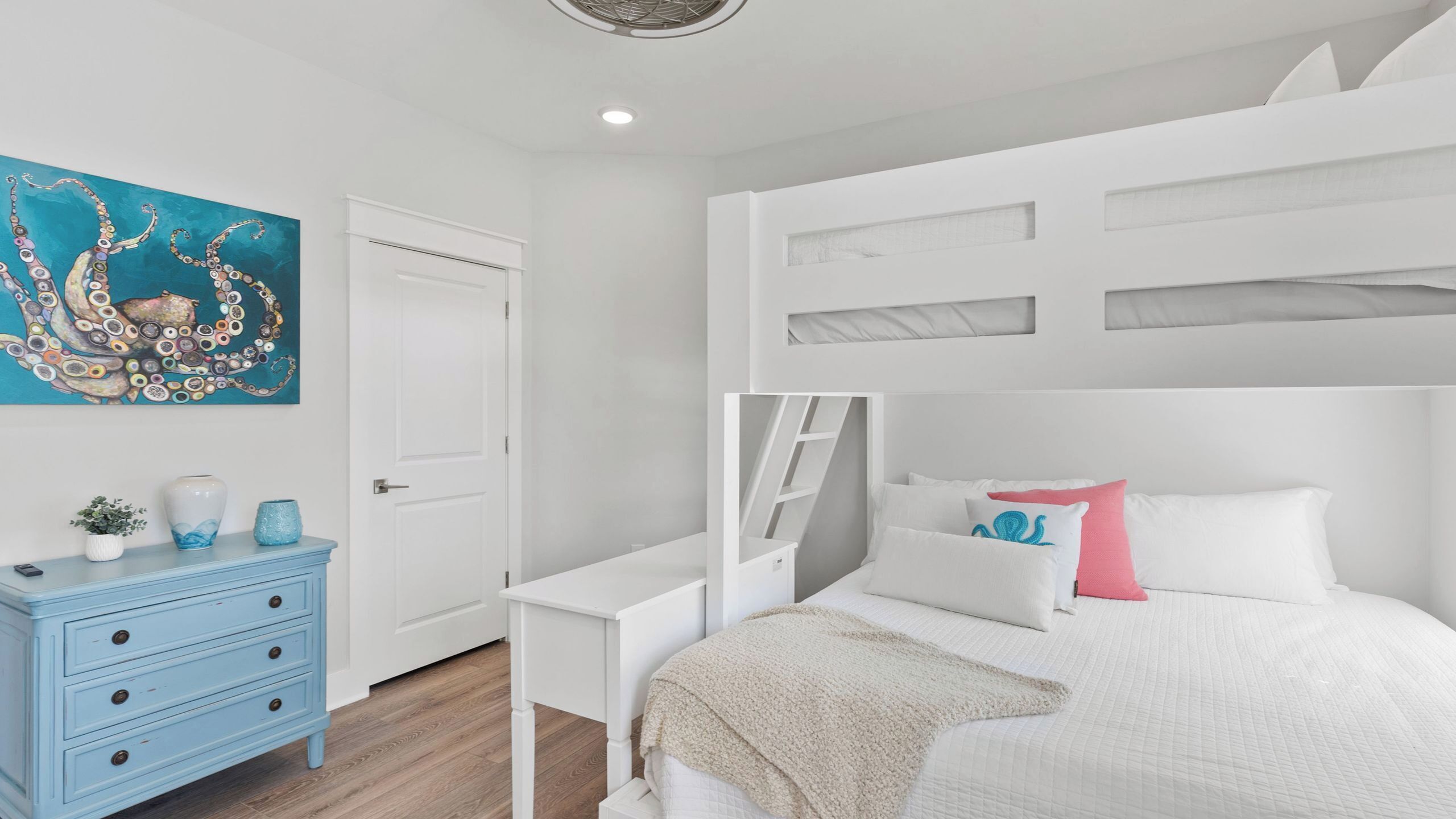 Quarto com cama de solteiro e beliche, escrivaninha, cômoda e pintura de polvo na parede.