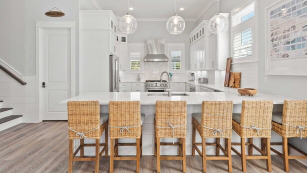 Une cuisine moderne avec des meubles blancs, un îlot central doté de tabourets de bar, des luminaires suspendus et une hotte de cuisine en acier inoxydable.