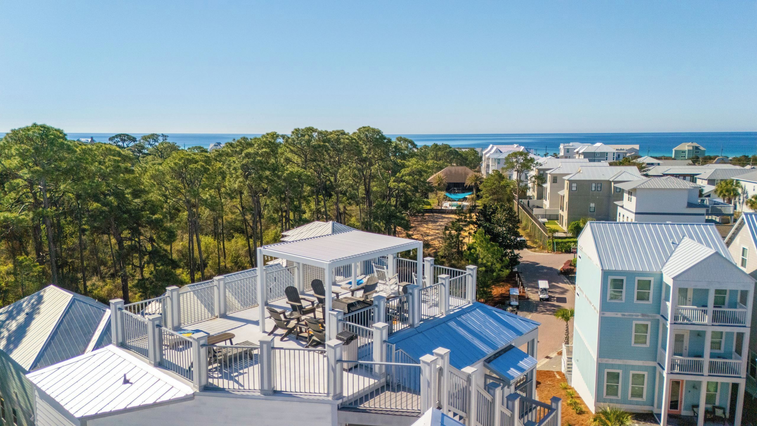 A coastal residential area with houses, a gazebo with outdoor seating, and a view of the ocean.
