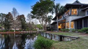 Ein modernes Haus mit einem großen Teich im Vorgarten, umgeben von Bäumen und einem gepflegten Rasen.