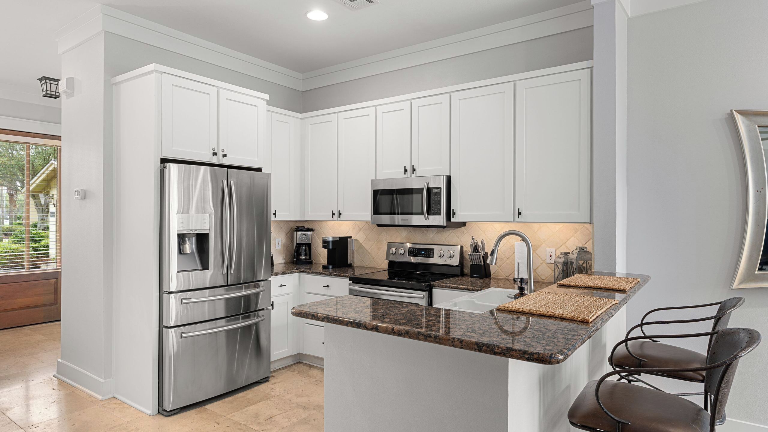 A modern kitchen with stainless steel appliances, white cabinetry, granite countertops, and a small island with seating.