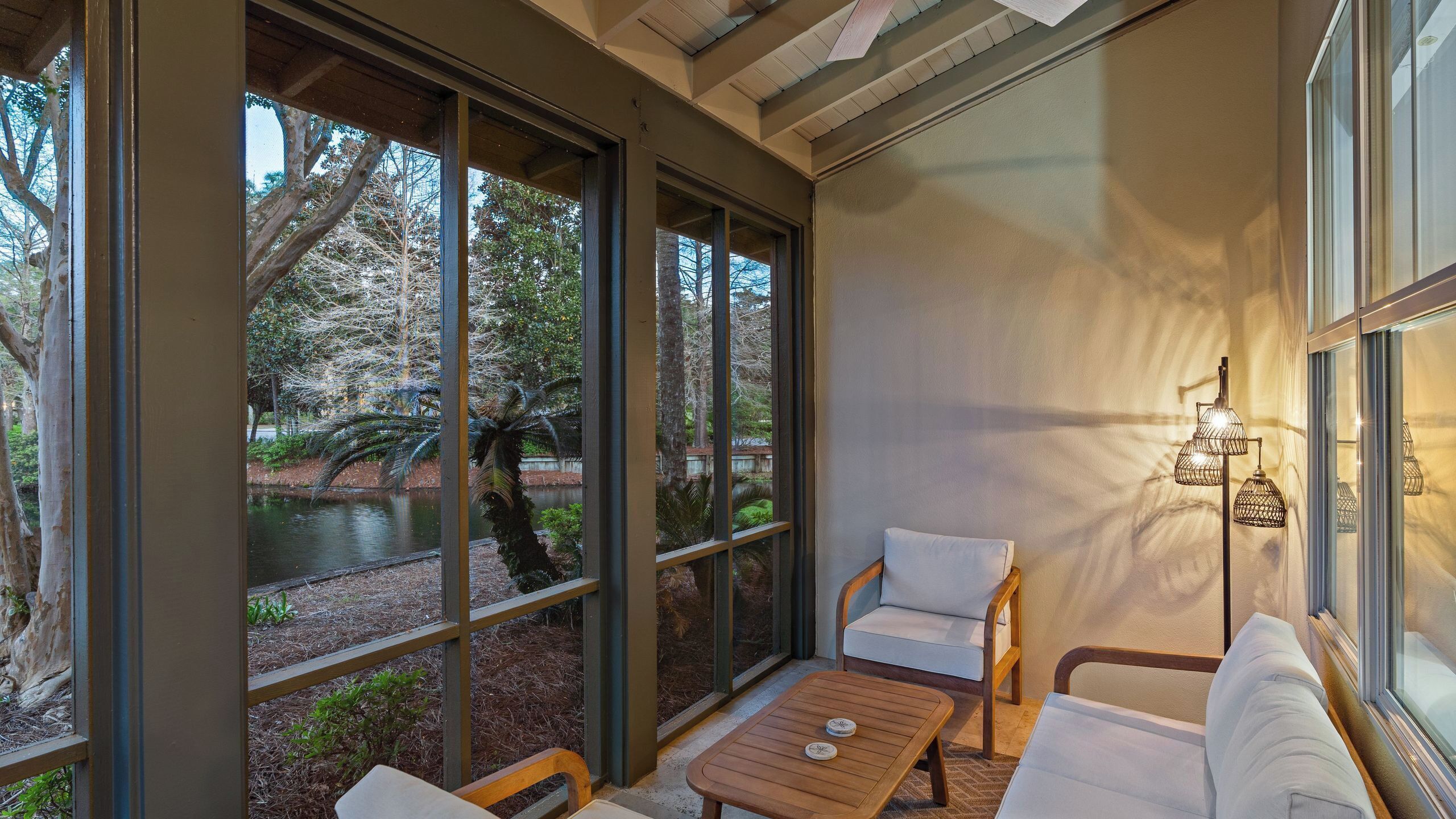 A room with large windows, a wooden table, a sofa, and a wall-mounted lamp.