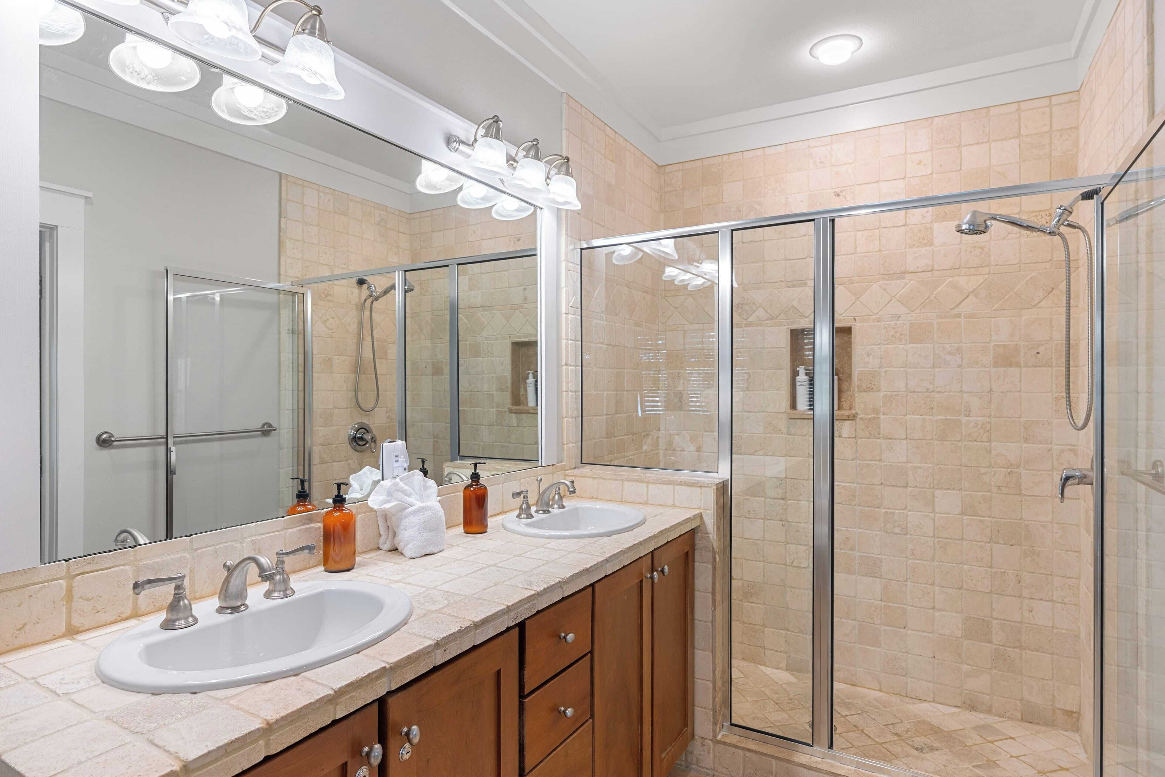 A modern bathroom with two sinks, a glass shower enclosure, and a large mirror with lights.