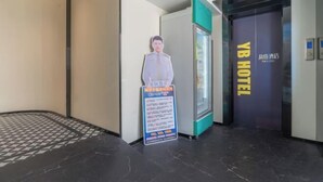Een hotelentree met een receptiebalie, een poster en een glazen lift.
