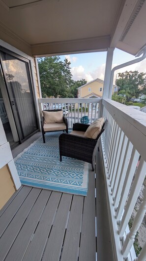 A covered porch with a patterned rug, two wicker chairs with cushions, and a view of a residential street.