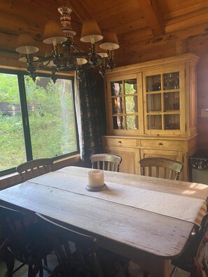 Enjoy a serene atmosphere with a view of the surrounding greenery from the large window, accompanied by a dining table for two and a traditional chandelier.