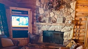 A cozy living room with leather sofas, a stone fireplace, and a television.