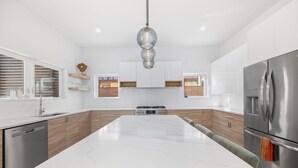 Une cuisine moderne avec des meubles blancs, un îlot central, des appareils en acier inoxydable et un luminaire suspendu.