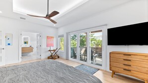 Une chambre moderne avec un grand lit, un ventilateur de plafond, une télévision et une porte-fenêtre coulissante donnant sur un balcon.