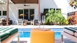 Un espace aménagé au bord de la piscine, avec des chaises longues et une table, une terrasse couverte et une vue sur la piscine.