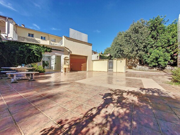 Un patio spacieux avec un sol carrelé, un espace salon couvert et une porte de garage.