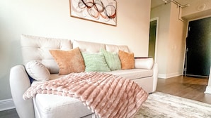A modern living room with a white sofa, multiple cushions, a large abstract painting, and a patterned rug. - Coastal Chic Apartment in St. Pete with Pool (St. Petersburg)