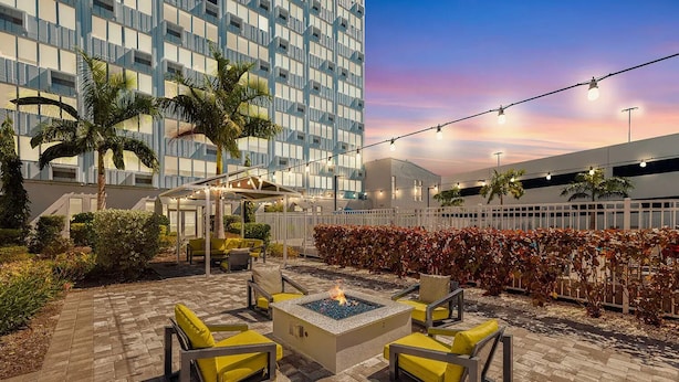 A patio area with outdoor seating, a fire pit, and a view of a modern building. - Coastal Chic Apartment in St. Pete with Pool (St. Petersburg)