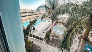 A view of a swimming pool area with lounge chairs and palm trees, surrounded by a building with multiple floors. - Coastal Chic Apartment in St. Pete with Pool (St. Petersburg)