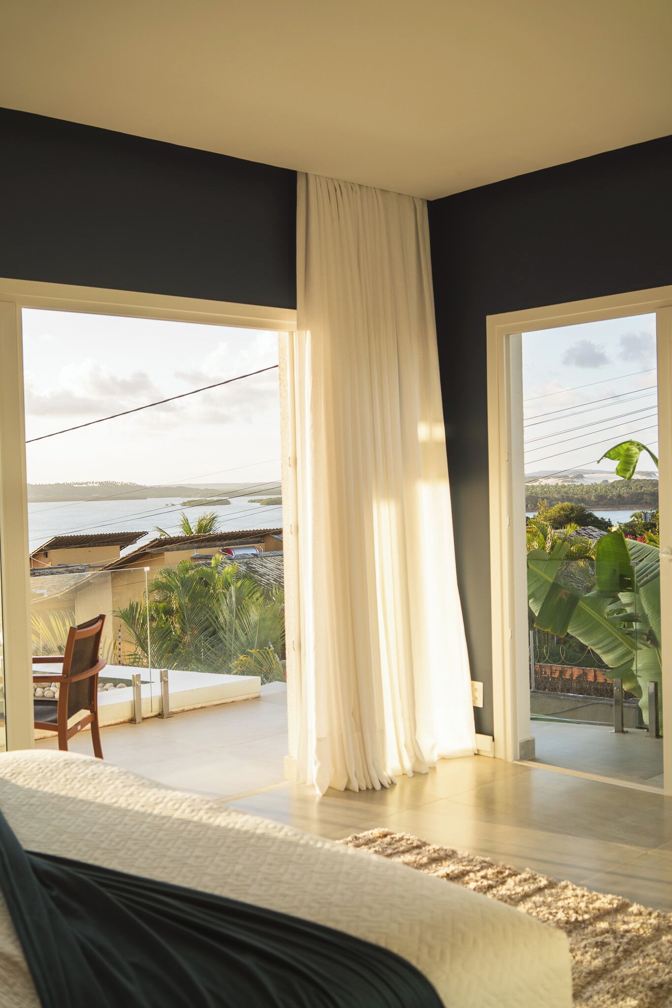 A bedroom with a large bed, a view of the sea, and a balcony with plants.