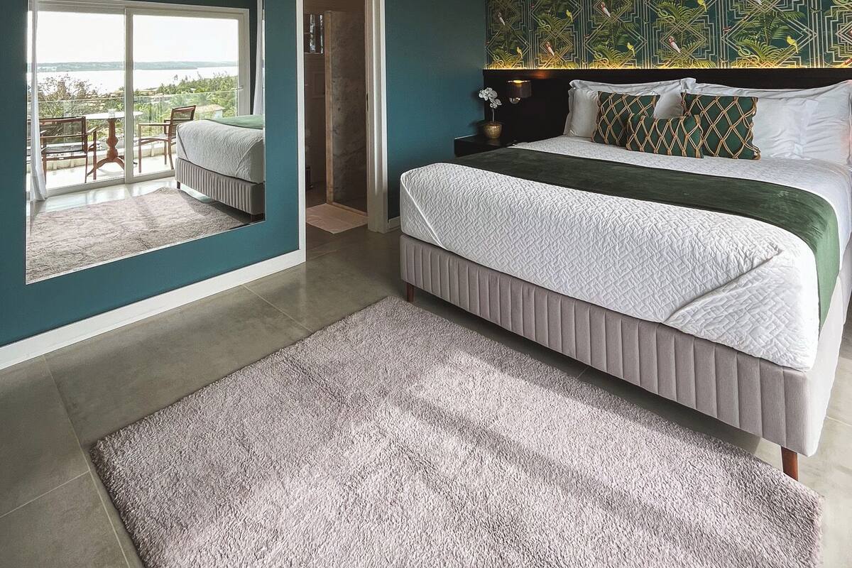 A bedroom with a large bed, a view through a window, and a door leading to a balcony.