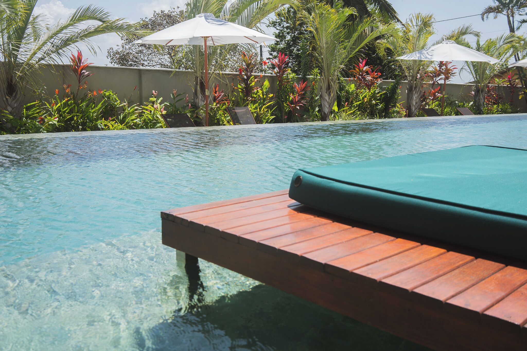 A clear pool with a wooden deck and a green mat.