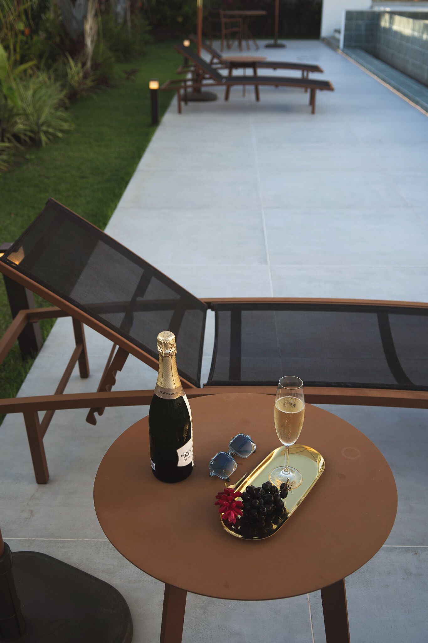 A table with a bottle of champagne, a glass of champagne, and a tray with grapes and sunglasses.