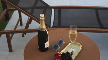 A table with a bottle of champagne, a glass of champagne, and a tray with grapes and sunglasses.