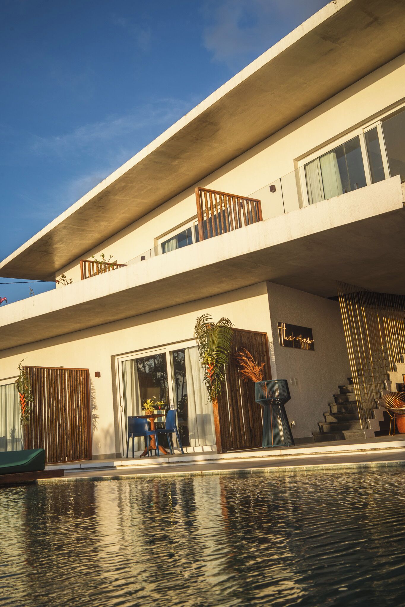 Un bâtiment moderne à deux étages, doté d’une piscine, d’un espace extérieur aménagé et d’une enseigne sur laquelle on peut lire : « la vue ».