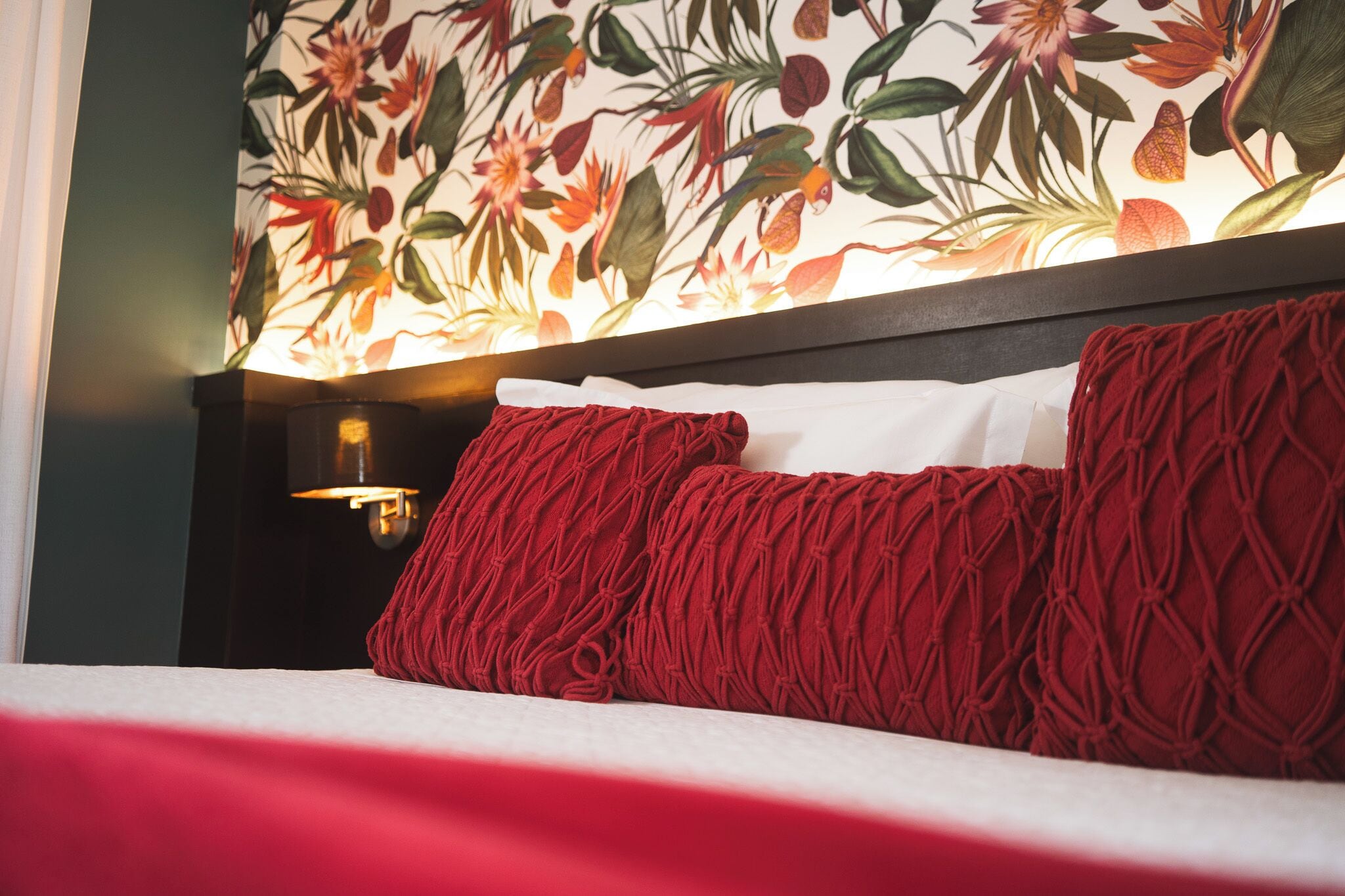 Un lit avec des oreillers rouges et un papier peint à motifs floraux.