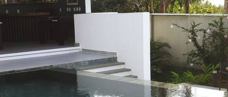 A modern outdoor pool area with clear water, a wooden deck, and a green cushioned lounge chair.