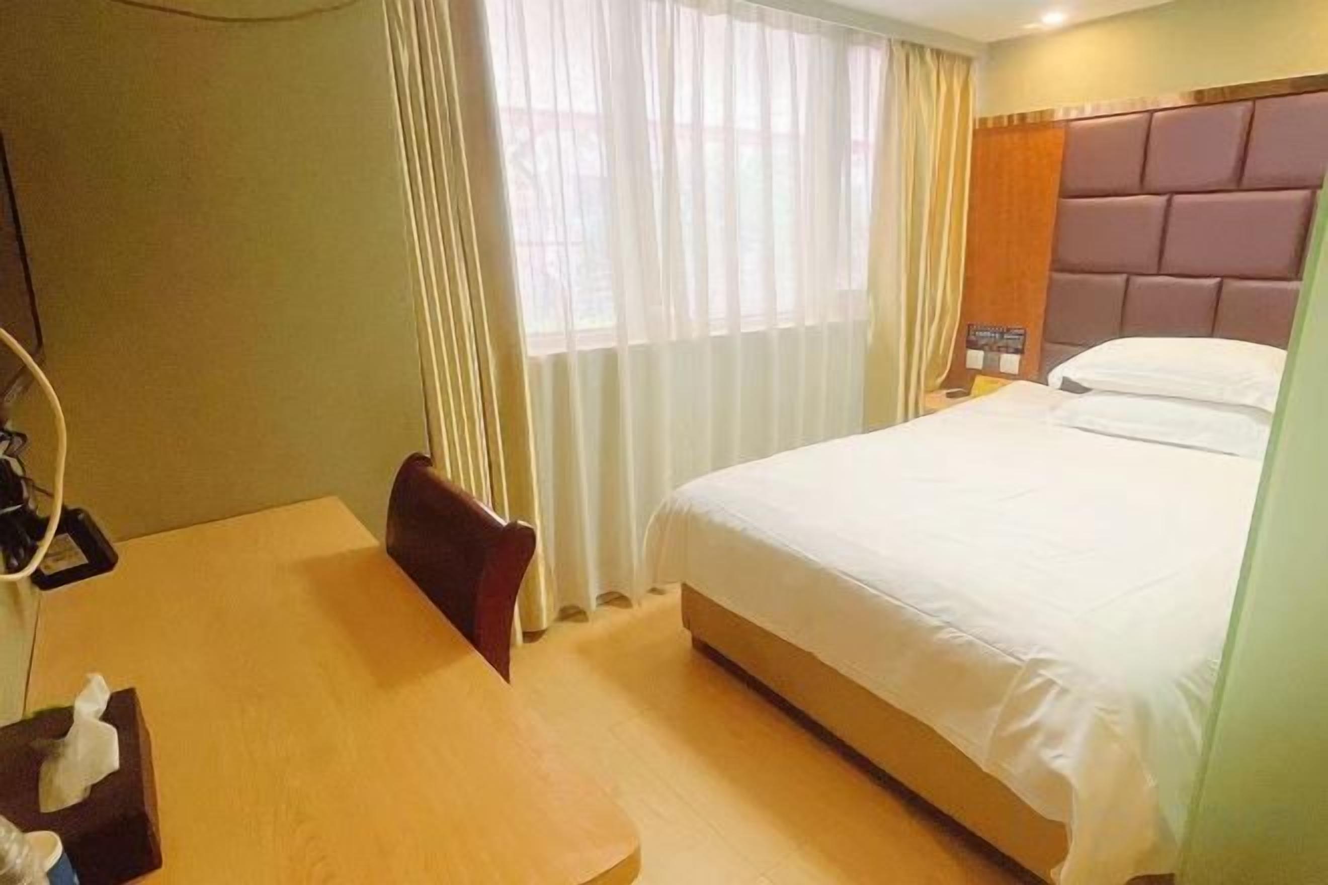 Una habitación de hotel con cama, mesita de noche, silla, escritorio y ventana con cortinas.