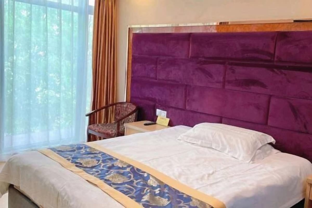 A hotel room with a large bed, a headboard, a chair, and a window.