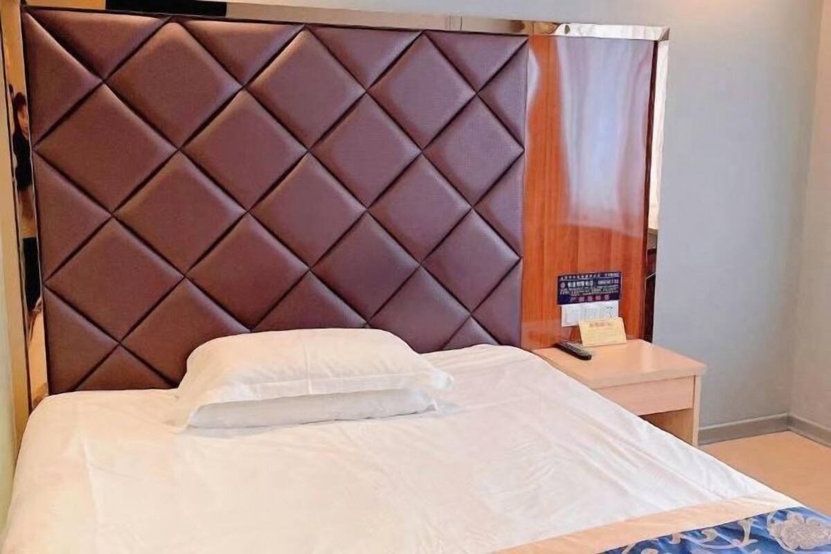 Una habitación de hotel con cabecera capitonada, una cama bien hecha con ropa de cama blanca y una mesita de noche pequeña con una lámpara.