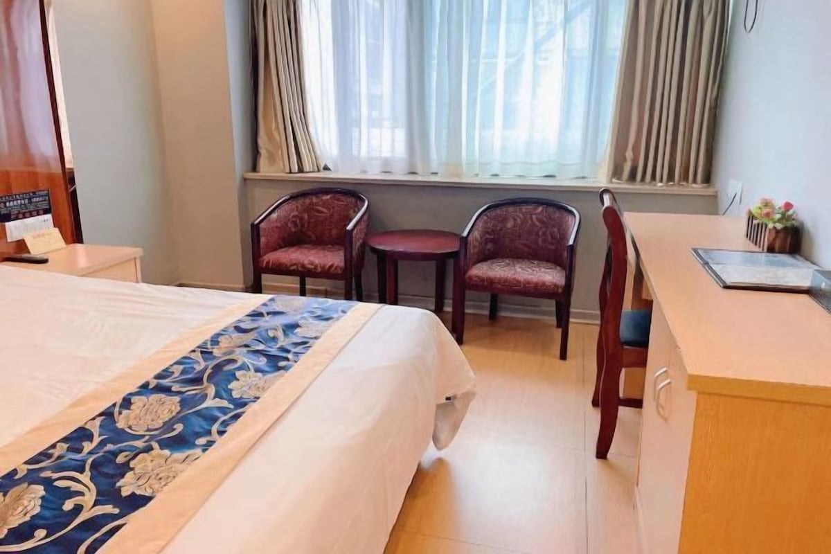 A hotel room with a bed, two chairs, a small table, and a window with curtains.
