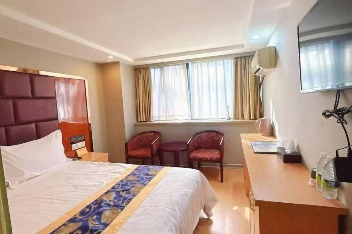 Habitación de hotel con cama, escritorio, dos sillas, televisor y ventana con cortinas.