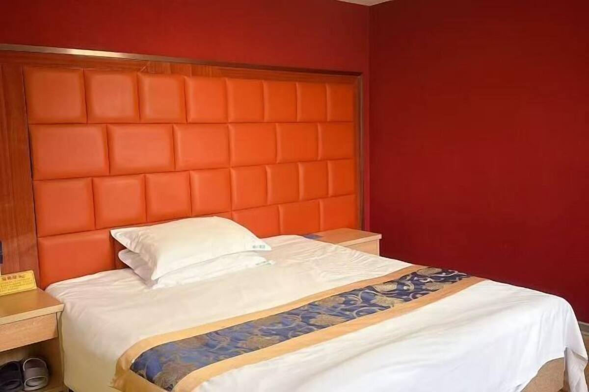 Habitación de hotel con pared roja, cabecera de madera, colcha blanca y un par de pantuflas en el suelo.