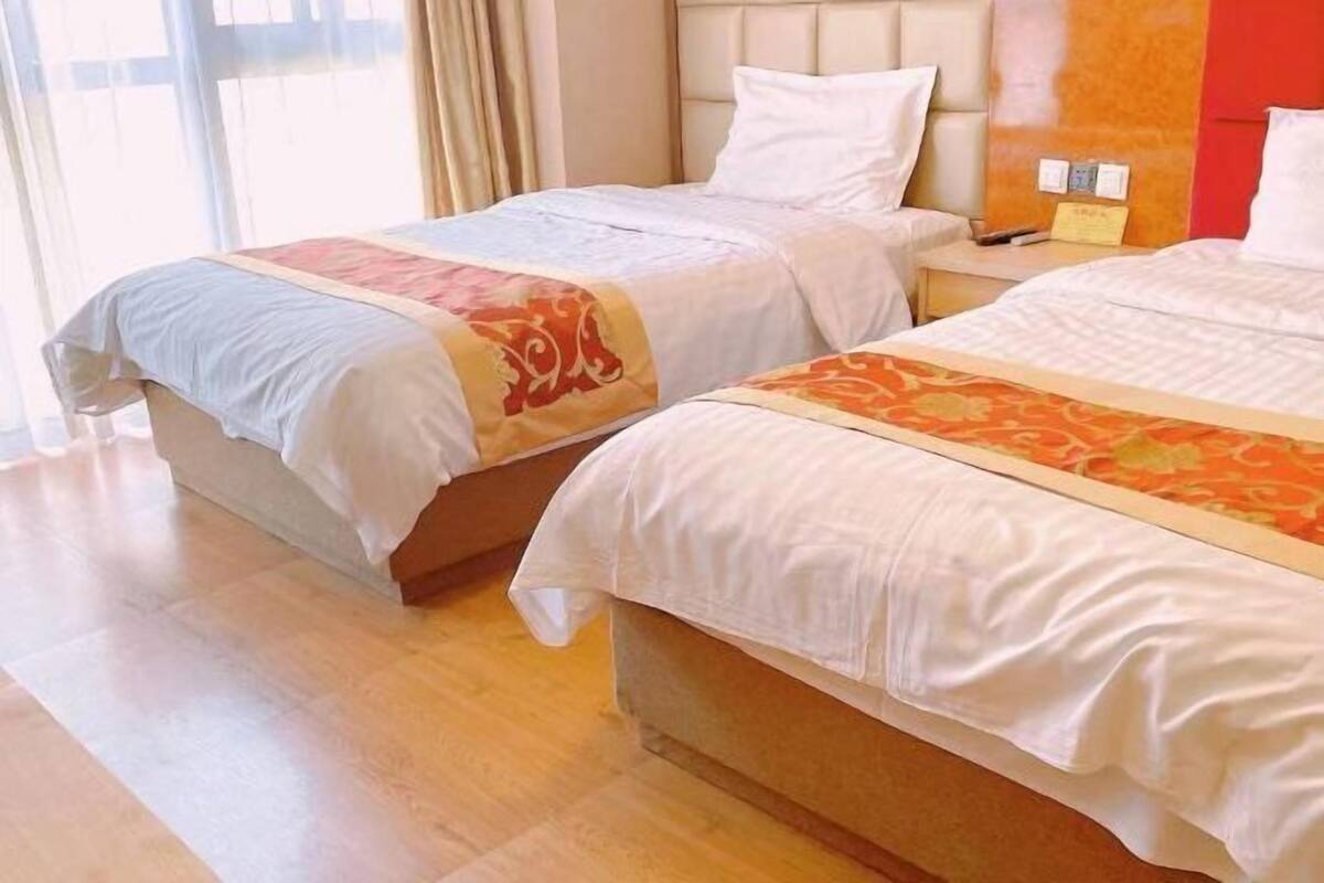 Habitación de hotel con dos camas, piso de madera y una ventana con cortinas.