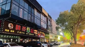 A building with illuminated signage, parked cars, and a tree-lined street.