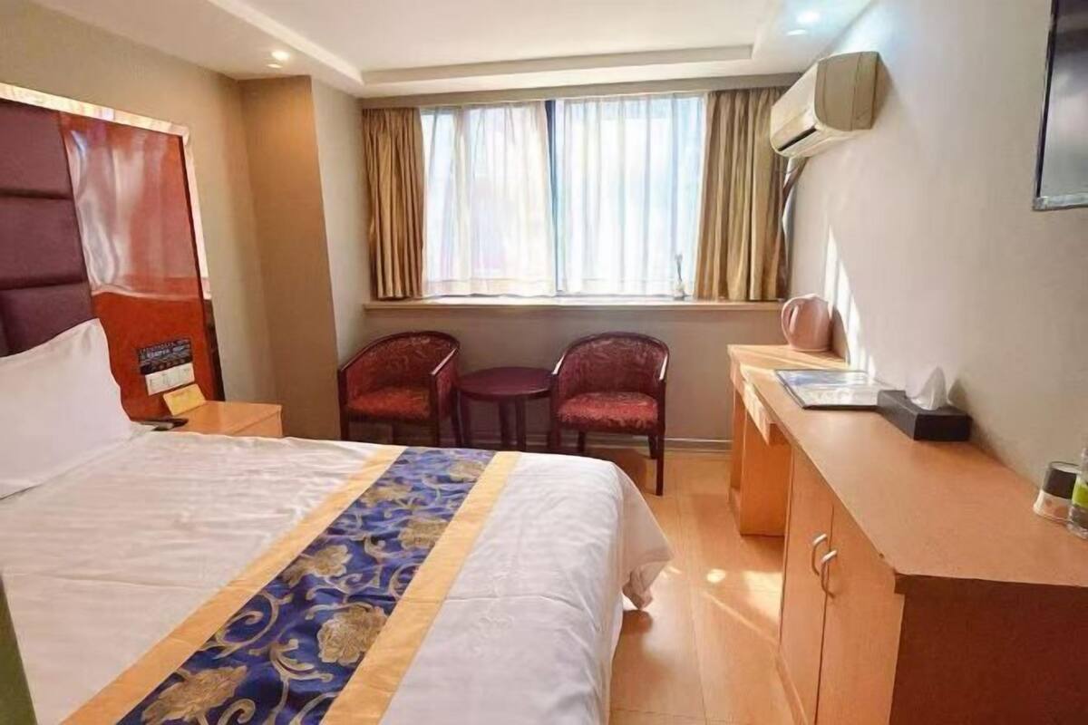 Una habitación de hotel con una cama grande, un escritorio, dos sillas, un ventanal con cortinas y un aire acondicionado de pared.
