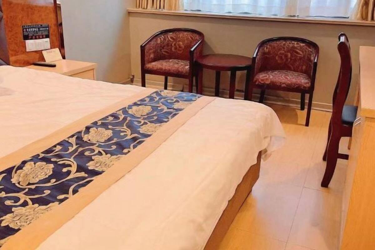 Una habitación de hotel con una cama, dos sillas, una mesita y un ventanal con cortinas.