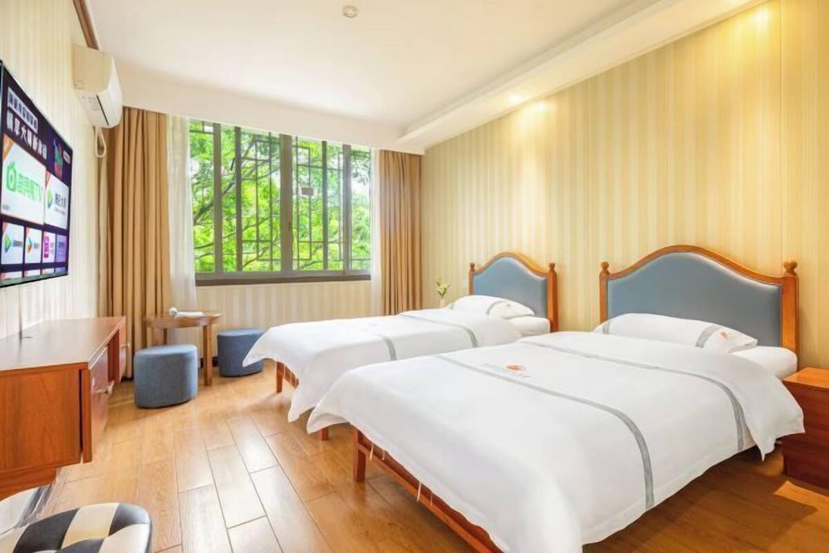 A hotel room with two beds, a desk, a chair, and a TV.