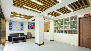 Eine Lobby mit einer Rezeption, einer Couch, einem Couchtisch und einem Regal mit Pflanzen.